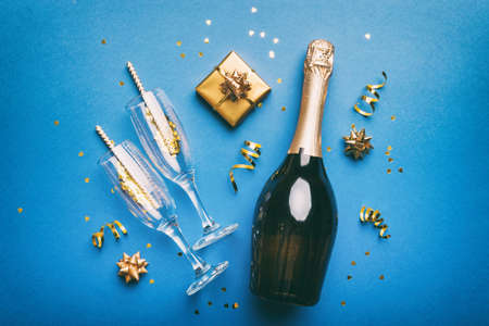 Bottle of champagne with colored glitter, confetti and gift box space for text on colorfull background, top view. Hilarious, christmas and birthday celebration.