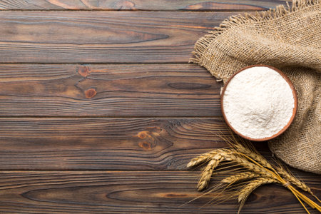 Flat lay of Wheat flour in wooden bowl with wheat spikelets on colored background. world wheat crisis.の写真素材