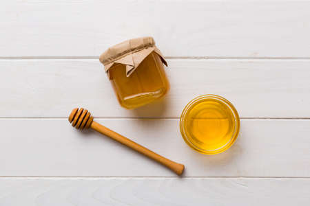 Glass jar of honey with wooden drizzler on colored background. Honey pot and dipper high above. Top view copy space.の写真素材