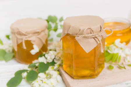 Sweet honey jar surrounded by spring acacia blossoms. Honey flows from a spoon in a jar. jars of clear fresh acacia honey on wooden background.の写真素材