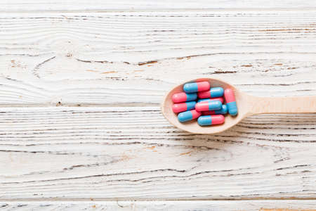 Vitamin capsules in a spoon on a colored background. Pills served as a healthy meal. Red soft gel...