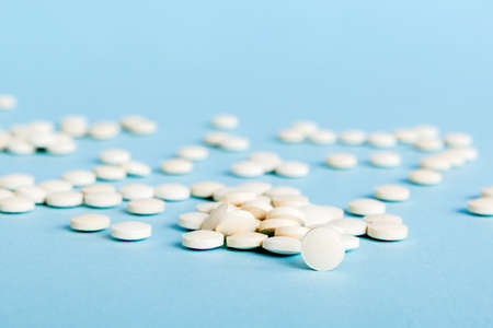 Heap of white pills on colored background. Tablets scattered on a table. Pile of red soft gelatin...