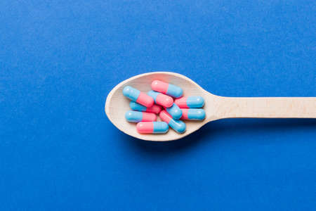 Vitamin capsules in a spoon on a colored background. Pills served as a healthy meal. Red soft gel...