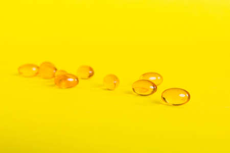 Heap of yellow pills on colored background. Tablets scattered on a table. Pile of red soft gelatin capsule. Vitamins and dietary supplements concept.の写真素材