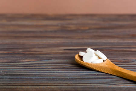 Heap of white pills on colored background. Tablets scattered on a table. Pile of red soft gelatin capsule. Vitamins and dietary supplements concept.の写真素材