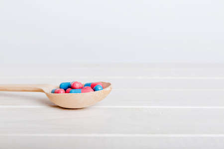 Vitamin capsules in a spoon on a colored background. Pills served as a healthy meal. Red soft gel...