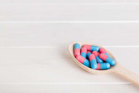 Vitamin capsules in a spoon on a colored background. Pills served as a healthy meal. Red soft gel...