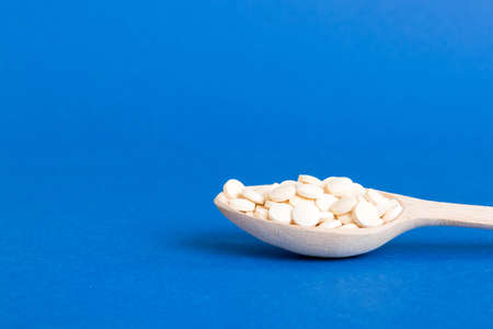 Heap of white pills on colored background. Tablets scattered on a table. Pile of red soft gelatin capsule. Vitamins and dietary supplements concept.の写真素材