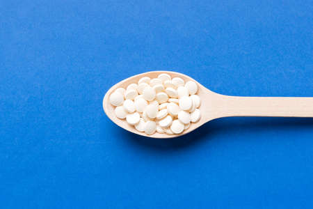 Heap of white pills on colored background. Tablets scattered on a table. Pile of red soft gelatin...