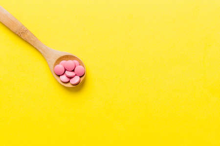 Vitamin capsules in a spoon on a colored background. Pills served as a healthy meal. Red soft gel vitamin supplement capsules on spoon.の写真素材