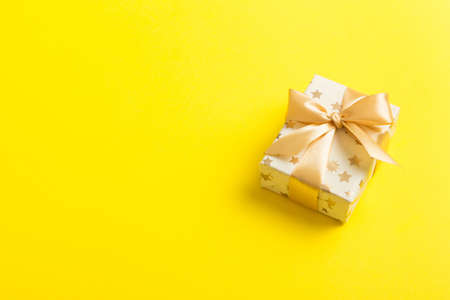 wrapped Christmas or other holiday handmade present in white paper with gold ribbon on colored background. Present box, decoration of gift on colored table, top view with copy space.の写真素材