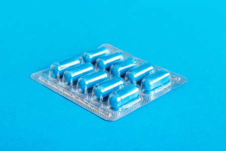 Blister package with Vitamin on color background. Medicine pills on a light background. Medicines and prescription pills flat lay background. blue medical tablets in blister.の写真素材