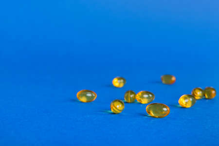 Heap of yellow pills on colored background. Tablets scattered on a table. Pile of red soft gelatin capsule. Vitamins and dietary supplements concept.の写真素材