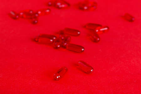 Heap of red pills on colored background. Tablets scattered on a table. Pile of red soft gelatin capsule. Vitamins and dietary supplements concept.の写真素材