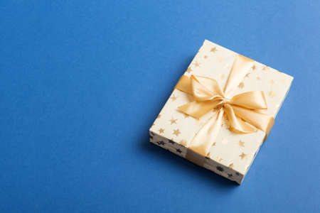 wrapped Christmas or other holiday handmade present in white paper with gold ribbon on colored background. Present box, decoration of gift on colored table, top view with copy space.の写真素材