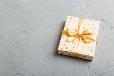 wrapped Christmas or other holiday handmade present in white paper with gold ribbon on colored background. Present box, decoration of gift on colored table, top view with copy space.の写真素材