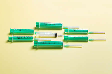 Top view of medical syringes with needles on yellow background with copy space. Injection treatment...