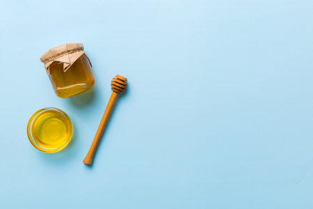 Glass jar of honey with wooden drizzler on colored background. Honey pot and dipper high above. Top view copy space.の写真素材