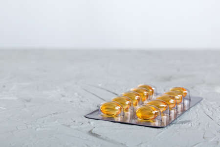 Blister package with fish oil capsules on color background. Medicine pills on a light background. Medicines and prescription pills flat lay background. Yellow medical tablets in blister.の写真素材