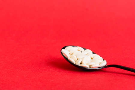Heap of white pills on colored background. Tablets scattered on a table. Pile of red soft gelatin capsule. Vitamins and dietary supplements concept.の写真素材