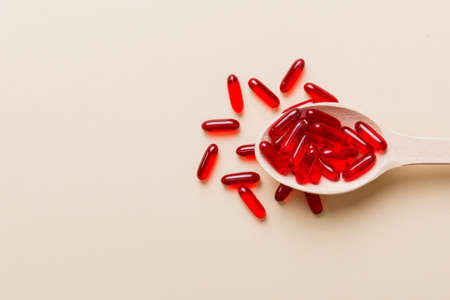 Vitamin capsules in a spoon on a colored background. Pills served as a healthy meal. Red soft gel vitamin supplement capsules on spoon.の写真素材