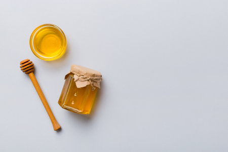 Glass jar of honey with wooden drizzler on colored background. Honey pot and dipper high above. Top view copy space.の写真素材