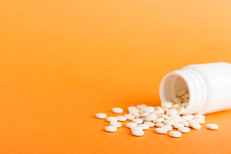 Medicine bottle and white pills spilled on a light background. Medicines and prescription pills flat lay background. White medical pills and tablets spilling out of a drug bottle.の写真素材