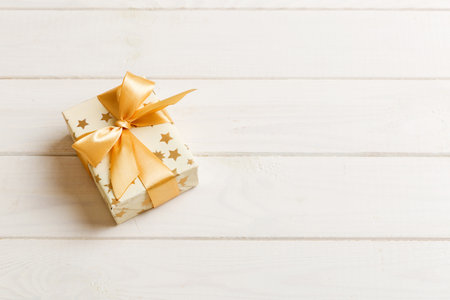 wrapped Christmas or other holiday handmade present in white paper with gold ribbon on colored...