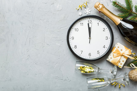 New year celebration concept with a bottle of champagne and two glasses toasting. Christmas gift box, alarm clock and fir tree branch on colored table. Top view copy space.の写真素材