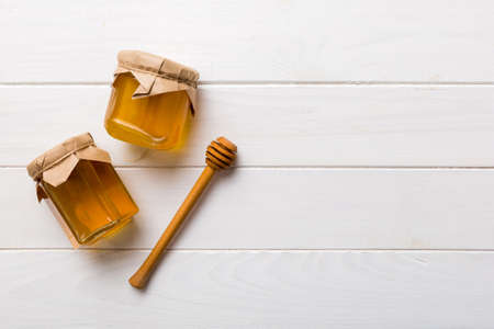 Glass jar of honey with wooden drizzler on colored background. Honey pot and dipper high above. Top view copy space.の写真素材