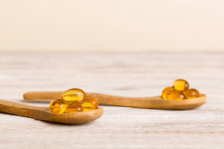 Vitamin omega capsules in a spoon on a colored background. Pills served as a healthy meal. Red soft gel vitamin supplement capsules on spoon.の写真素材