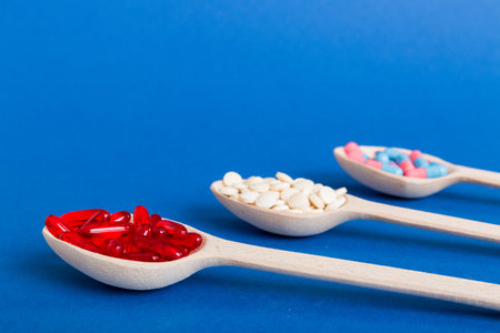 Vitamin capsules in a spoon on a colored background. Pills served as a healthy meal. Red soft gel...