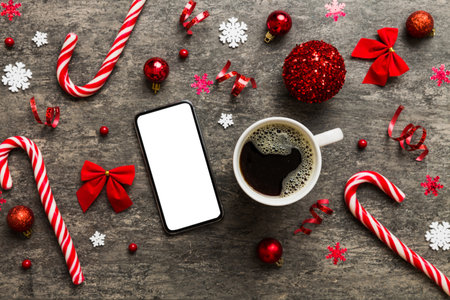 top view of smart phone with hot cup of coffee. Christmas decoration on colored background.