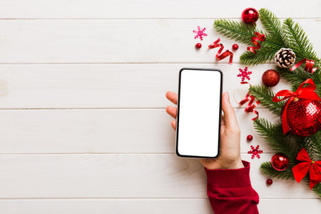 christmas mockup with space for text. christmas advertising app template. hand holding phone with empty screen on table background. Happy New Year and Xmas Flat lay.の写真素材