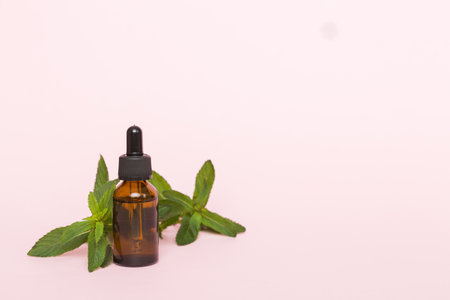Natural Mint Essential Oil in a Glass Bottle. organic cosmetics with herbal extracts of mint on colored background.の写真素材