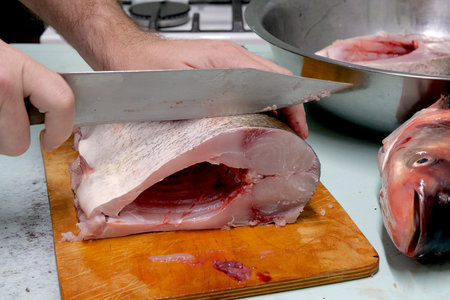 Man prepares fresh silver carp fish. Cuts it into steaks with a knife. home cooking concept.