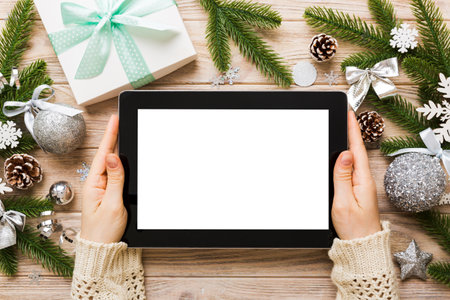 Christmas online shopping from home, female hands holding tablet pc with blank white display top view. woman hand holding tablet with blank screen, Christmas tree and gifts on background.の写真素材
