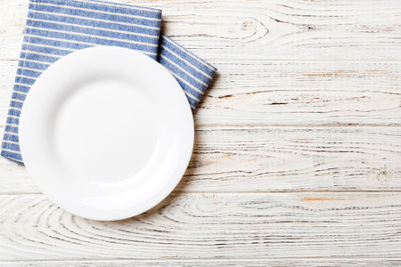Top view on colored background empty round white plate on tablecloth for food. Empty dish on napkin...