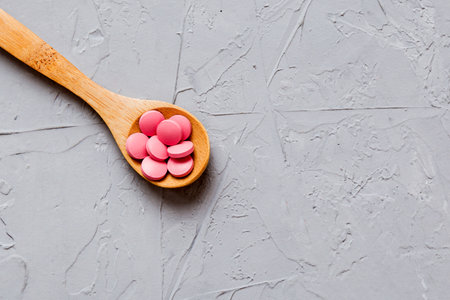 Vitamin capsules in a spoon on a colored background. Pills served as a healthy meal. Red soft gel vitamin supplement capsules on spoon.の写真素材