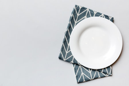 Top view on colored background empty round white plate on tablecloth for food. Empty dish on napkin...