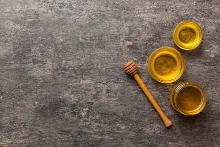 Glass jar of honey with wooden drizzler on colored background. Honey pot and dipper high above. Top view copy space.の写真素材
