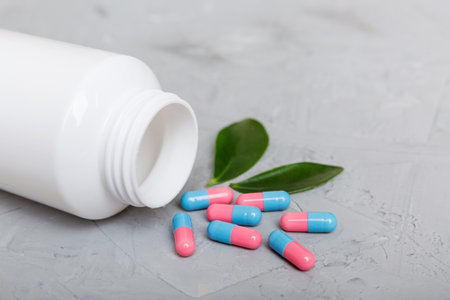 different drugs and health supplement pills poured from a medicine bottle health care and medical top view on colored background.の写真素材