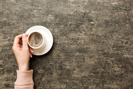 Minimalistic style woman hand holding a cup of coffee on Colored background. Flat lay, top view cappuccino cup. Empty place for text, copy space. coffee addiction. Top view, flat lay.の写真素材