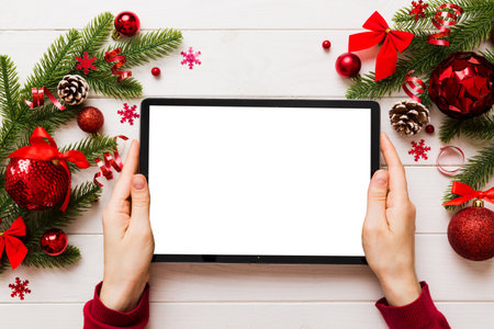 Christmas online shopping from home, female hands holding tablet pc with blank white display top view. woman hand holding tablet with blank screen, Christmas tree and gifts on background.の写真素材