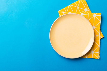 Top view on colored background empty round yellow plate on tablecloth for food. Empty dish on napkin...