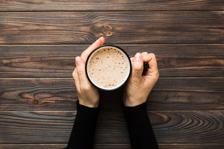 Minimalistic style woman hand holding a cup of coffee on Colored background. Flat lay, top view cappuccino cup. Empty place for text, copy space. coffee addiction. Top view, flat lay.の写真素材