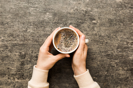 Minimalistic style woman hand holding a cup of coffee on Colored background. Flat lay, top view cappuccino cup. Empty place for text, copy space. coffee addiction. Top view, flat lay.の写真素材