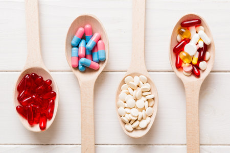 Vitamin capsules in a spoon on a colored background. Pills served as a healthy meal. Red soft gel vitamin supplement capsules on spoon.の写真素材