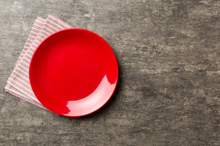 Top view on colored background empty round red plate on tablecloth for food. Empty dish on napkin with space for your design.の写真素材