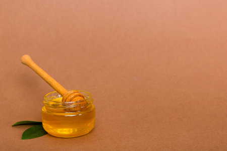 Honey in jar with leaves and honey dipper on colored background top view with copy text.の写真素材